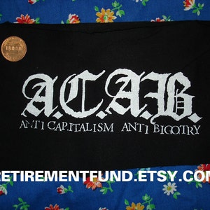Könnte beinhalten: Schwarzer Stoff-Patch mit weißer Aufschrift "A.C.A.B. ANTI CAPITALISM ANTI BIGOTRY".