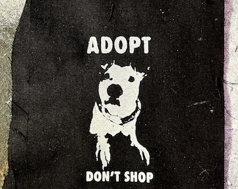 May include: Black fabric patch with white text that reads "Adopt Don't Shop" and a white silhouette of a dog's head.