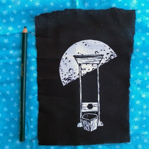 May include: A black fabric patch with a white design of a guillotine with a crescent moon above it.