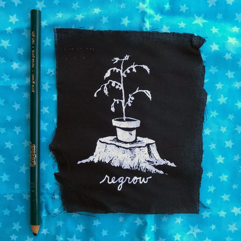 Może przedstawiać: Czarny materiałowy znaczek z białą ilustracją rośliny w doniczce rosnącej z pnia drzewa. Tekst "regrow" jest napisany pod rośliną.