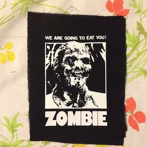 Pode incluir: Patch de ferro-on preto e branco com um rosto de zumbi e o texto "WE ARE GOING TO EAT YOU!" e "ZOMBIE".
