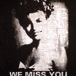 May include: A black and white image of a person with the text "WE MISS YOU" printed below.