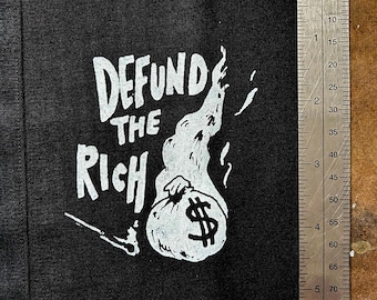 May include: Black fabric patch with white text and graphic. The text reads "Defund the Rich" and the graphic is a burning bag of money with a dollar sign.