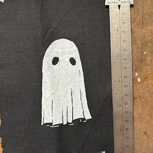 Peut inclure: Un patch en tissu noir avec un motif de fantôme blanc. Le fantôme a deux yeux et une forme simple et arrondie.