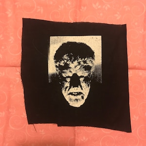 May include: A black fabric patch with a white image of a werewolf's face.