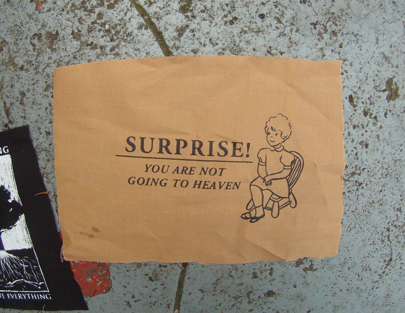 May include: A brown paper sign with the text "SURPRISE! YOU ARE NOT GOING TO HEAVEN" and a black and white illustration of a girl sitting on a chair.