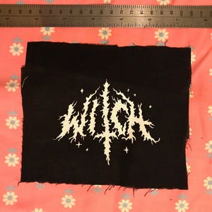 May include: Black fabric patch with a white embroidered design of the word "WITCH" in a stylized font. The design includes small stars around the word.