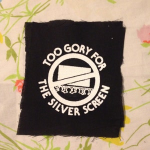 May include: Black fabric patch with white text and a graphic. The text reads "Too Gory For The Silver Screen" with a circle and diagonal line through it.