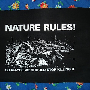 May include: Black patch with white text that reads "NATURE RULES! SO MAYBE WE SHOULD STOP KILLING IT". The patch features a black and white image of a forest.