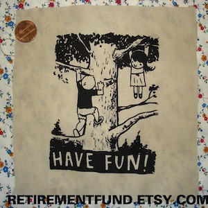 May include: Black and white illustration of two figures hanging from a tree branch. The text "HAVE FUN!" is printed below the figures. The illustration is printed on a beige fabric.