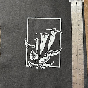 May include: Black fabric patch with a white outline of a flower with five petals. The flower is surrounded by leaves and is centered on the patch. The patch is 4 inches by 4 inches.