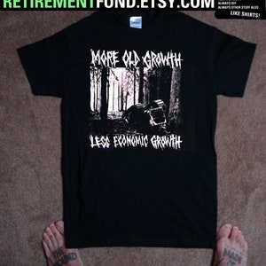 May include: Black t-shirt with a graphic featuring a forest scene and the text "MORE OLD GROWTH" above and "LESS ECONOMIC GROWTH" below. The shirt is laid flat on a brown surface.