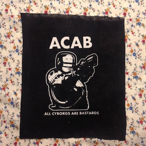 May include: Black and white patch with the text "ACAB" and the words "All Cyborgs Are Bastards" below. The patch features a stylised image of a cyborg holding a gun.
