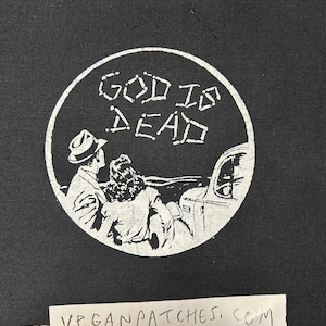 Puede incluir: Parche bordado en blanco y negro con un diseño circular. El círculo presenta una pareja en un automóvil con el texto "God is Dead" encima.