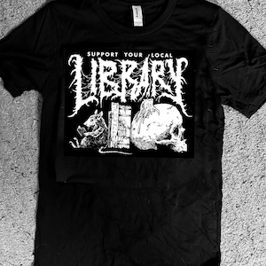 May include: Black t-shirt with a white graphic that reads "SUPPORT YOUR LOCAL LIBRARY" in a gothic font. The graphic features a rat, a skull, and a stack of books. The shirt is made of a soft material.