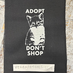 May include: Black and white iron-on patch with a kitten and the text "Adopt Don't Shop" and the website "veganpatches.com".