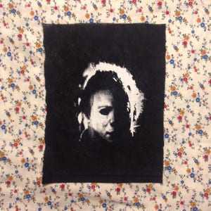 Pode incluir: Patch termocolante preto e branco com um close-up do rosto de Michael Myers da franquia de filmes de terror Halloween.