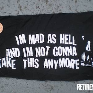 May include: Black fabric patch with white text that reads "I'm mad as hell and I'm not gonna take this anymore". A white silhouette of a person with arms raised is in the top right corner.