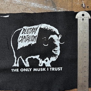 May include: Black and white patch with a cartoon musk ox wearing a sign that says "DESTROY CAPITALISM". The text "THE ONLY MUSK I TRUST" is below the image.