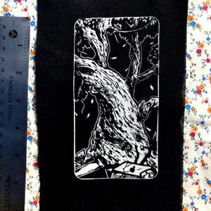 May include: A black and white rectangular patch depicting a detailed illustration of a large tree with a textured trunk and branches. The design includes falling leaves and a partial moon. The patch is on black fabric.