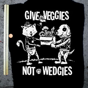 May include: Black and white illustration of a cat and dog carrying a box of vegetables. The text "GIVE VEGGIES NOT WEDGIES" is printed below the image. The text "RETIREMENT FUND" is printed at the bottom of the image.