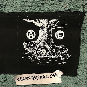 Pode incluir: Etiqueta de ferro de passar a ferro preto e branco com uma árvore a crescer de um carro. O carro tem a palavra "Police" escrita no lado. A árvore tem dois círculos com as letras "A" e "E" neles.