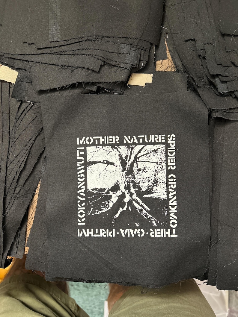May include: Black and white patch with the text "MOTHER NATURE'S SPIDER GRANDMOTHER", "THIEVES. VIVA. WHIRLWIND", and "KOKYANGVULT" printed on it. The patch features a black and white image of a tree with roots.
