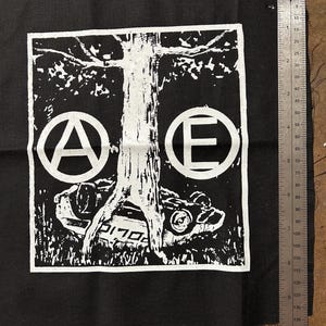 May include: Black and white patch with a tree, a car, and the letters "A" and "E" in circles. The letters are stylized and look like anarchy symbols.