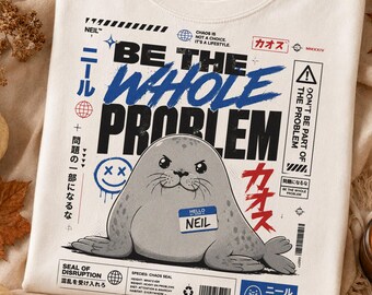 May include: A cream-colored t-shirt featuring a graphic of a gray seal wearing a name tag that says NEIL. The text reads BE THE WHOLE PROBLEM, along with various Japanese characters, symbols, and technical-style design elements in black, blue, and red.
