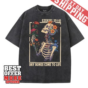 May include: Dark gray t-shirt featuring a skeleton design with colorful flowers and the text "EZEKIEL 37:1-10" and "DRY BONES COME TO LIFE". The shirt has a vintage wash.