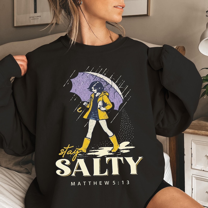 May include: Black sweatshirt with a graphic of a person walking in the rain under an umbrella. The person is wearing a yellow jacket and boots. The text "stay SALTY" and "MATTHEW 5:13" are below the graphic.