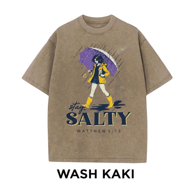 May include: Khaki-colored t-shirt with a graphic of a person walking in the rain under a purple umbrella. The text "stay SALTY" and "MATTHEW 5:13" are below the graphic. The words "WASH KAKI" are at the bottom.