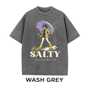 May include: Wash grey t-shirt with a graphic of a person walking in the rain under an umbrella. The design includes the words "stay SALTY" and "MATTHEW 5:13". The person is wearing a yellow jacket and boots.