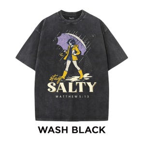 May include: Wash black t-shirt with a graphic of a person walking in the rain under an umbrella. The person is wearing a yellow jacket and boots. The text "stay SALTY" and "MATTHEW 5:13" are below the graphic.
