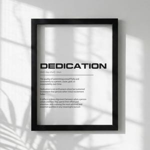 May include: A framed print with the definition of "DEDICATION" in black text on a white background. The definition includes the word's pronunciation and a detailed explanation of its meaning. The frame is black.
