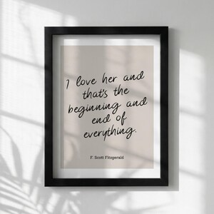 May include: A framed print with the quote "I love her and that's the beginning and end of everything" by F. Scott Fitzgerald. The text is in a handwritten style, set against a beige background, and framed in black.