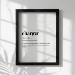 May include: A framed print with the word "charger" in a bold, black font. Below the word is the phonetic pronunciation and a definition that reads: "the one item that is never where you left it, never long enough, and always borrowed by someone who 'just needed a second.'"