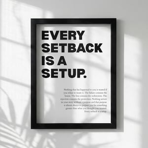 May include: Black framed print with the text "EVERY SETBACK IS A SETUP." The print also includes a paragraph of text below the main phrase. The background is white.
