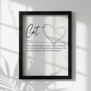 May include: A framed print with the word "Cat" in elegant script, accompanied by a heart outline. The text below defines a cat as a source of mystery, comfort, and love, promising a calmer and more beautiful life.
