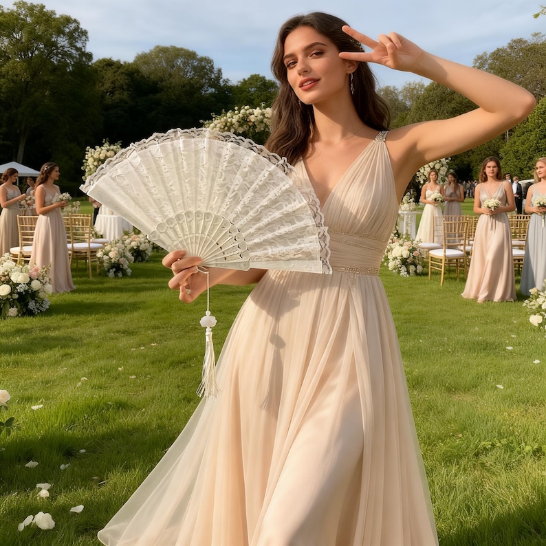 以下が含まれることがあります： 明るいピーチ色のフォーマルドレスを着た女性が、タッセル付きの白いレースの扇子を持っています。扇子は開いており、その複雑なデザインが明らかになっています。同様のドレスを着た他の女性が背景に立っており、結婚式やフォーマルなイベントを示唆しています。
