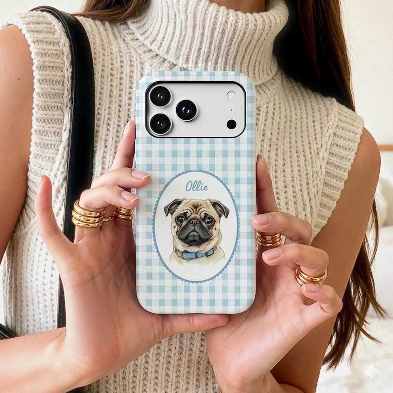 Op de afbeelding: Een lichtblauw en wit telefoonhoesje met een gingham-patroon en een centraal ovaal embleem met een geschulpte rand. In het embleem staat een gedetailleerde illustratie van een beige mopshond met een blauwe halsband en de naam Ollie.