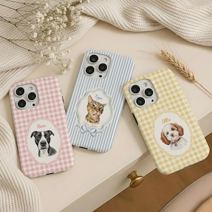 Op de afbeelding: Drie smartphonehoesjes met aangepaste huisdierportretten. Het linkerhoesje heeft een roze gingham-patroon met een zwart-witte hond genaamd Rosie. Het middelste hoesje heeft blauwe verticale strepen met een kat genaamd Tiger. Het rechterhoesje heeft een geel gingham-patroon met een bruin-witte hond genaamd Ollie.