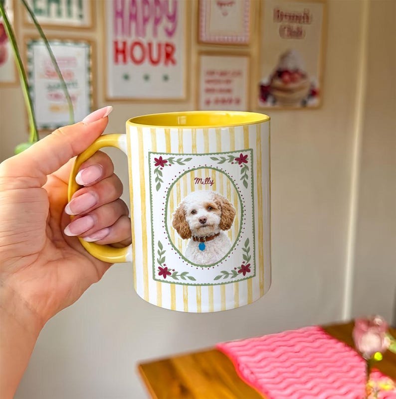 Puede incluir: Una taza de cer&aacute;mica con un patr&oacute;n de rayas verticales amarillas y blancas. El frente presenta un marco rectangular con un borde floral que contiene una fotograf&iacute;a de un perro blanco con el nombre Milly impreso encima. La taza tiene un asa amarilla.