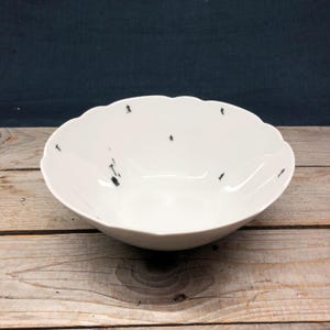 May include: A white ceramic bowl with a scalloped rim. The bowl is decorated with a black and white design of skiers on a snowy mountain.