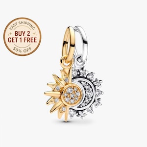 Puede incluir: Un colgante de amuleto de dos tonos con un diseño de sol y luna. El lado del sol es dorado con detalles de cristal transparente, mientras que el lado de la luna es plateado con adornos de cristal similares. El amuleto tiene una fianza dorada.