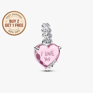 May include: A pink heart-shaped charm with the words "I LOVE YOU" inscribed. The charm has a silver-colored bail with clear, round accents. The charm is a romantic jewelry item.