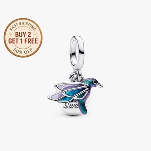 Può includere: Un charm a forma di colibrì in argento, con dettagli in smalto iridescenti blu, viola e verde. Il charm ha una piccola base rotonda con la scritta "Sweet" ed è sospeso a un anello d'argento. Le ali del colibrì sono spiegate.