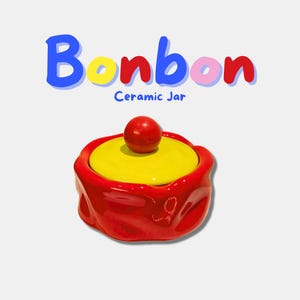 Puede incluir: Un tarro de cerámica rojo con tapa amarilla y pomo rojo. El tarro está etiquetado como "Bonbon Ceramic Jar" en texto colorido. El tarro tiene forma redondeada y acabado brillante.