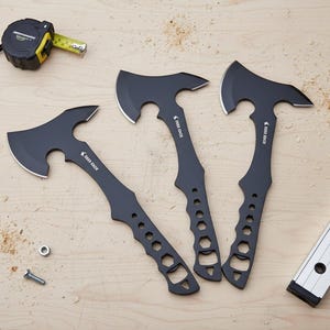 May include: Three black hatchets with silver blades and the text "DEER EDGE" are arranged on a wooden surface. A tape measure, screws, and a level are also present. The hatchets have a unique handle design.
