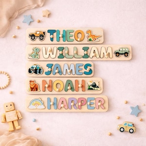 K&ouml;nnte beinhalten: F&uuml;nf Holz-Namenspuzzles mit den Namen THEO, WILLIAM, JAMES, NOAH und HARPER. Jedes Puzzle enth&auml;lt bunte, ausgeschnittene Buchstaben mit kleinen Holzkn&ouml;pfen, verziert mit Illustrationen von Fahrzeugen, Dinosauriern, einem B&auml;ren, Bergen und einem Regenbogen.